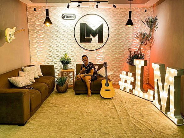 Foto do cantor sergipano, Luanzinho Moraes em seu estúdio, sentado com o violão
